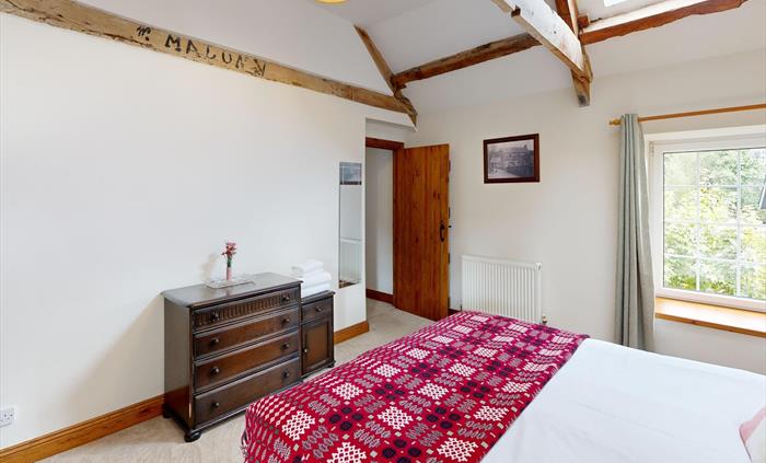 A spacious king-size bedroom with exposed beams, heritage furniture, and a red traditional Welsh tapestry blanket adding warmth and character.